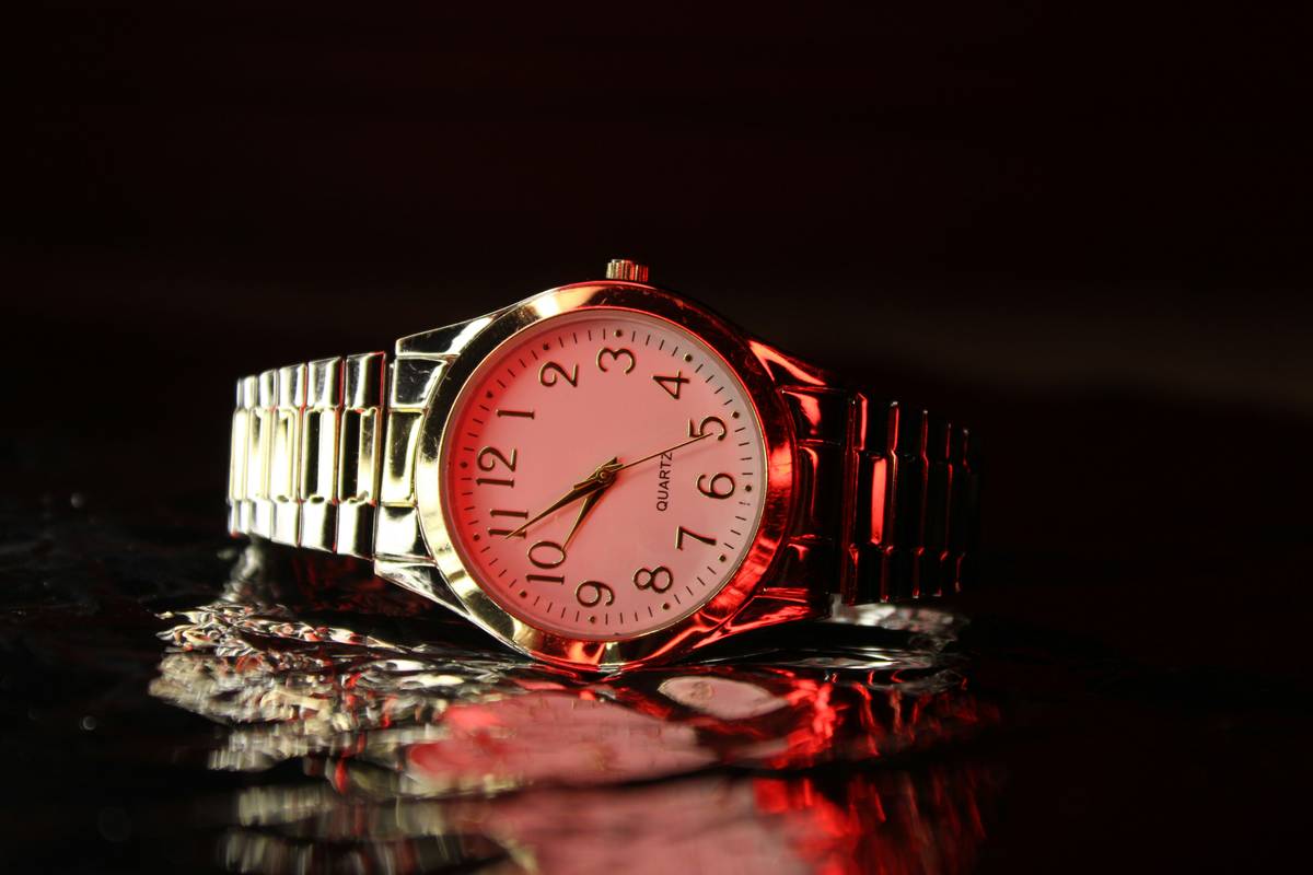 A woman wearing a champagne dress holding a copper-tone watch near the beach at sunset